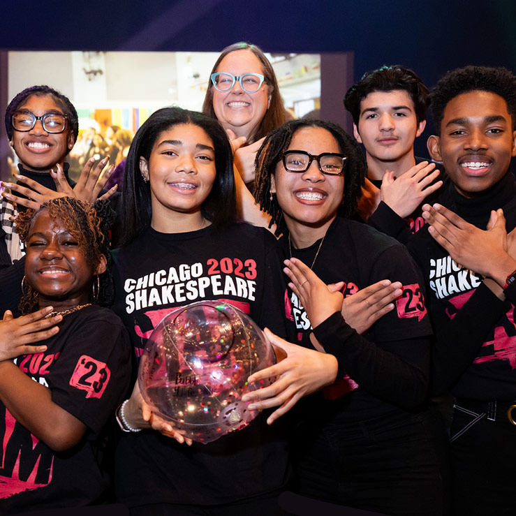  A group of seven smiling individuals, wearing black "CHICAGO 2023 SHAKESPEARE SLAM" T-shirts, pose together with one holding a balloon.
