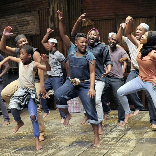 A group of nine people energetically dancing on a wooden floor.