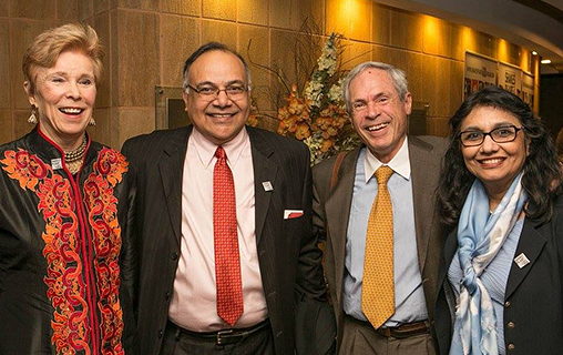  Four smiling adults in semi-formal attire standing closely together indoors under warm lighting. 