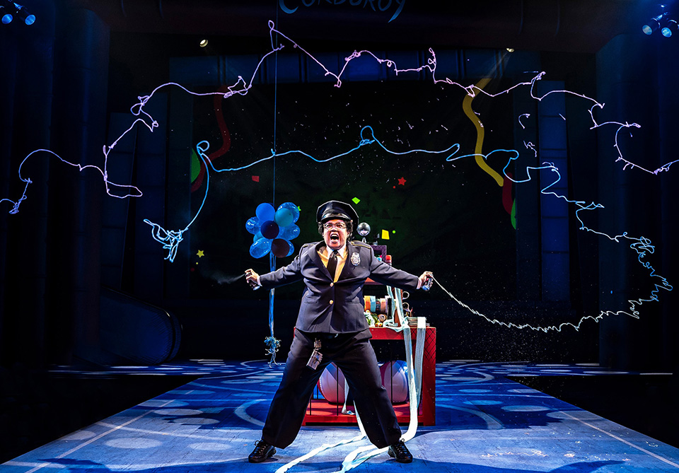 Performer in a security guard uniform with outstretched arms on a colorful and dynamic stage.