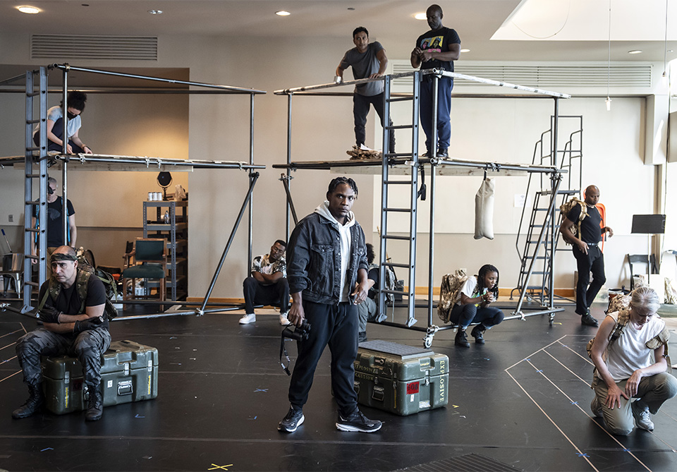 People in a rehearsal space with metal scaffolding structures, engaged in various activities.