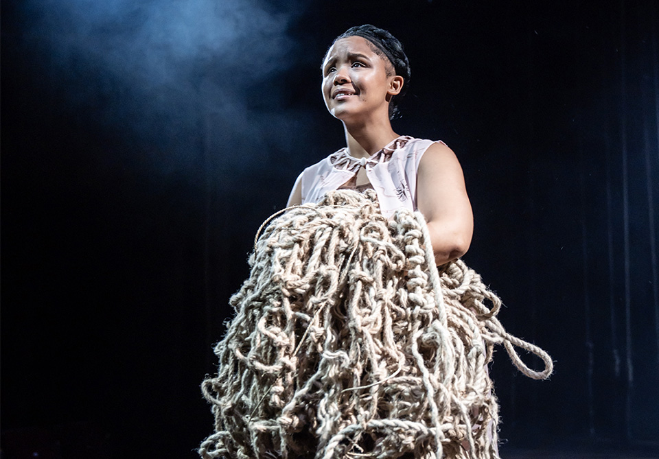 Person holding a large, tangled mass of thick rope against a dark, dramatic background.