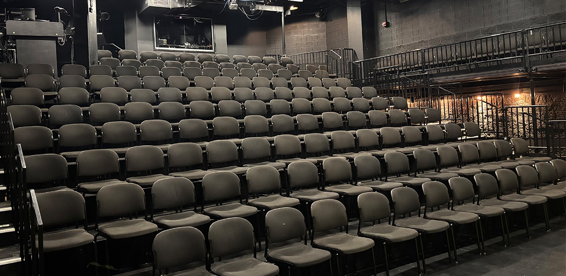 Black and white photo of a modern theater with tiered seating, balcony seating, and industrial-style design.