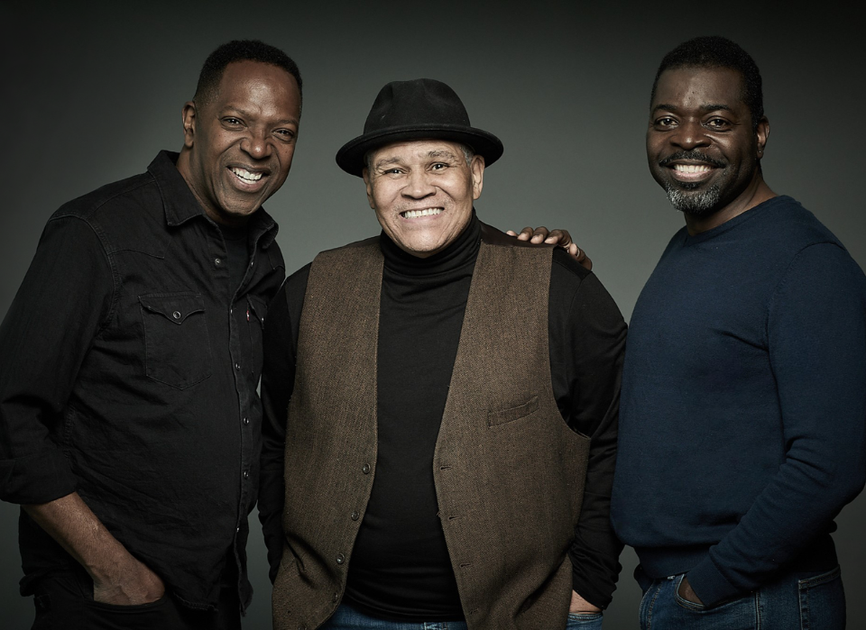 Three men smiling at the camera against a dark background.