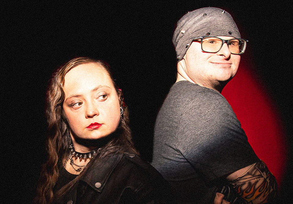 Two people standing back-to-back against a dark background with a red spotlight.