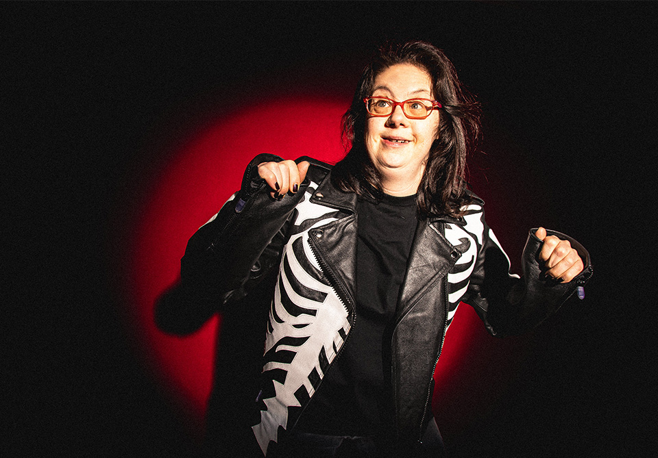 A person wearing a black leather jacket with a skeleton design, standing against a dark background with a red halo effect.