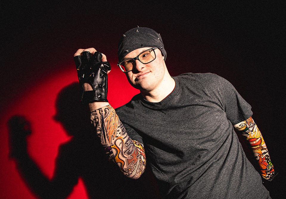 Person with tattoos and a studded glove against a red background.