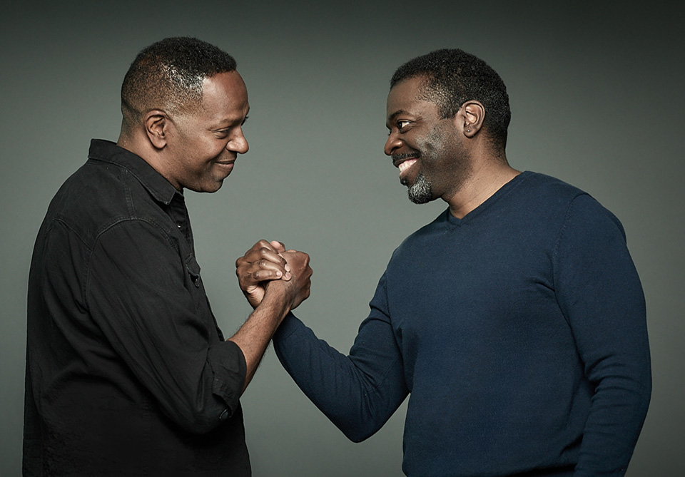 Two smiling individuals shaking hands against a gray background.