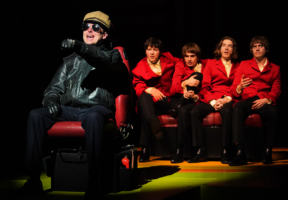 An individual in a leather jacket and cap gesturing as if driving, with four others in red jackets seated behind.