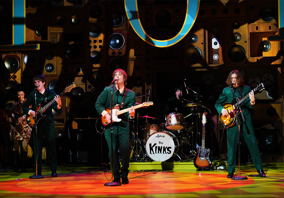 A band performs energetically on stage with vintage speaker backdrop.