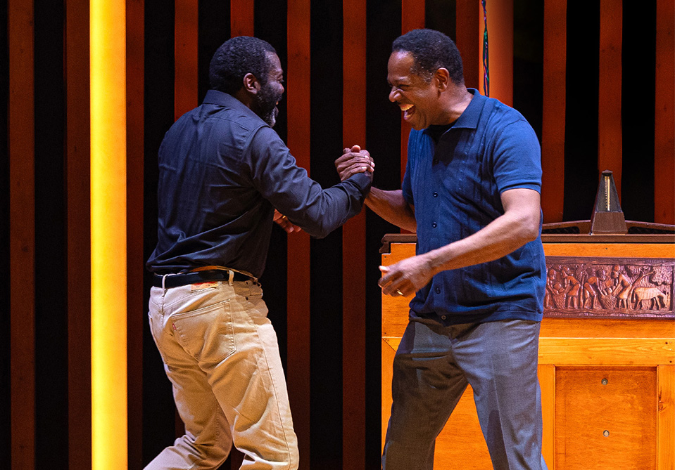 Two men in dark blue shirts smiling and embracing in a handshake 