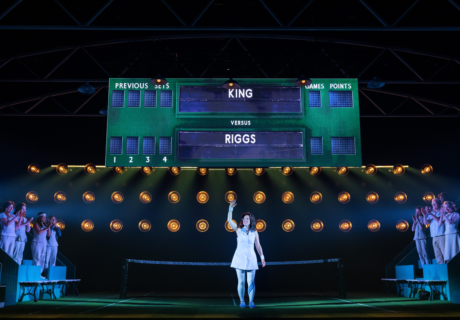 Stage set with tennis-themed elements, a scoreboard, and a person waving.