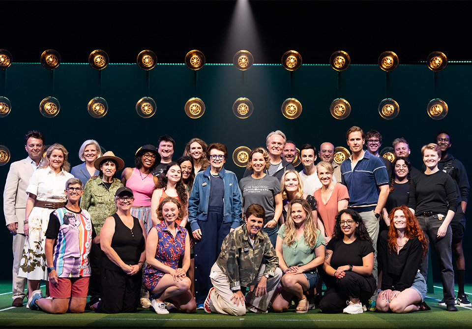 Group of people from the company of "Billie Jean" pose for a photo on stage with Billie Jean King and wife Ilana Kloss
