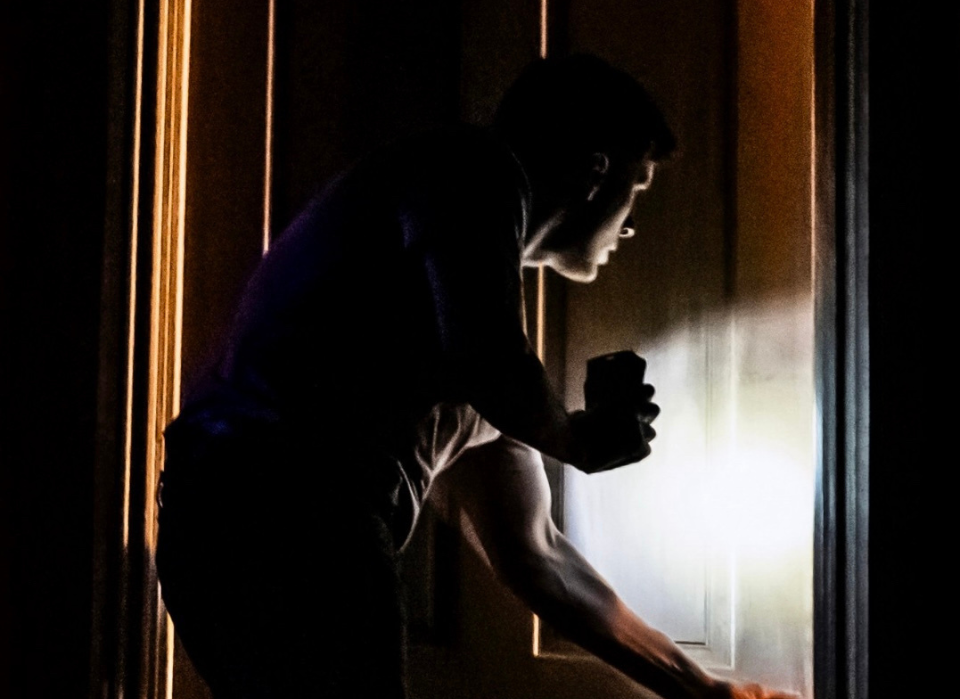 A silhouette of a person opening a door with a flashlight in a dimly lit scene.