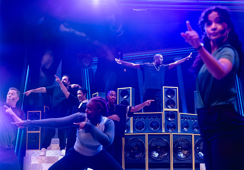 Performers on stage gesturing energetically with large speakers in the background.