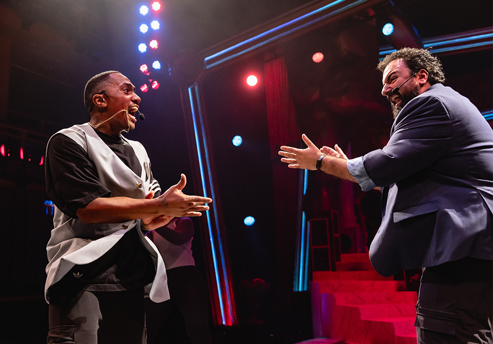 Two performers on stage with colorful lights and a dramatic setting.
