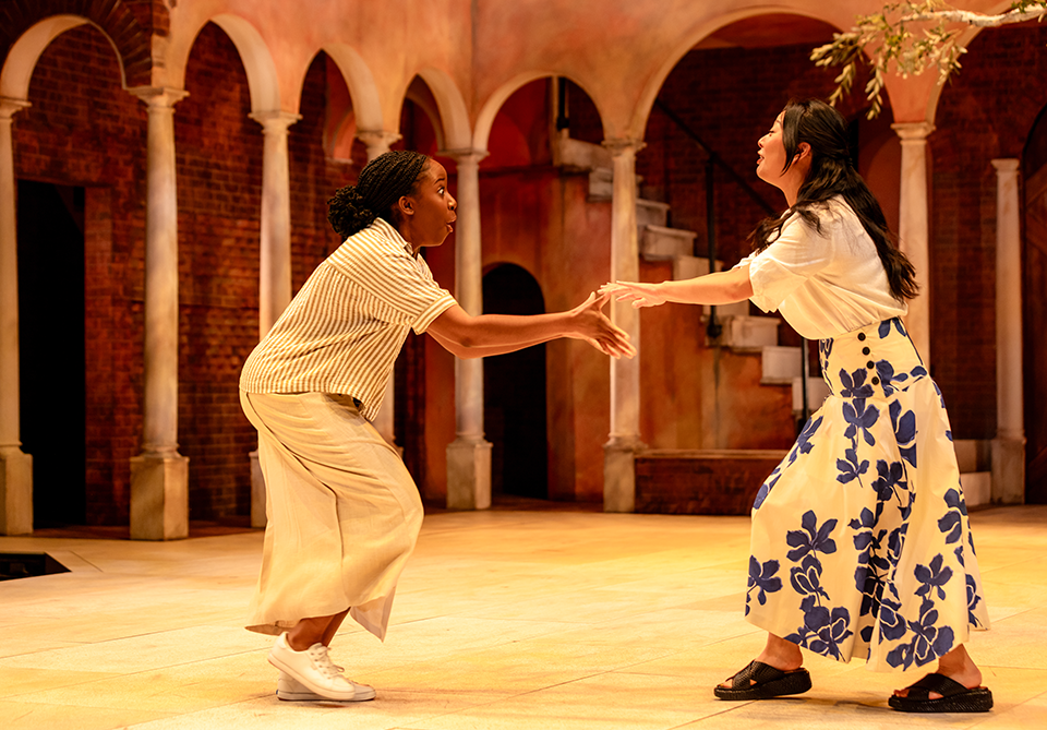 Two people on a stage with Mediterranean-style arches, reaching towards each other.