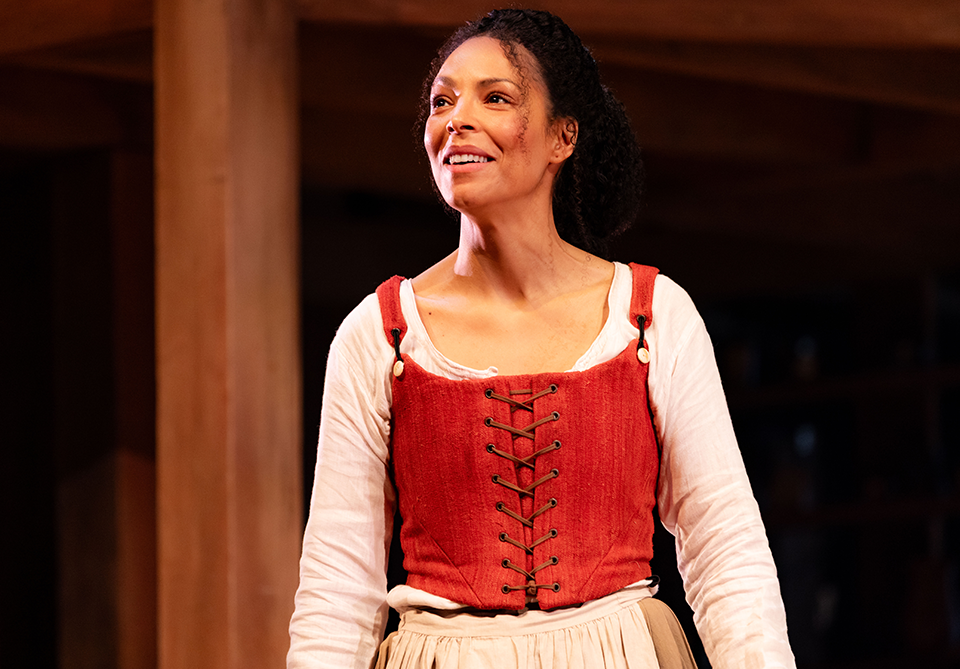 A young woman on a stage in old-English costume staring out into the crowd