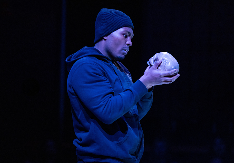 Person in a dark hoodie and beanie holding a skull.