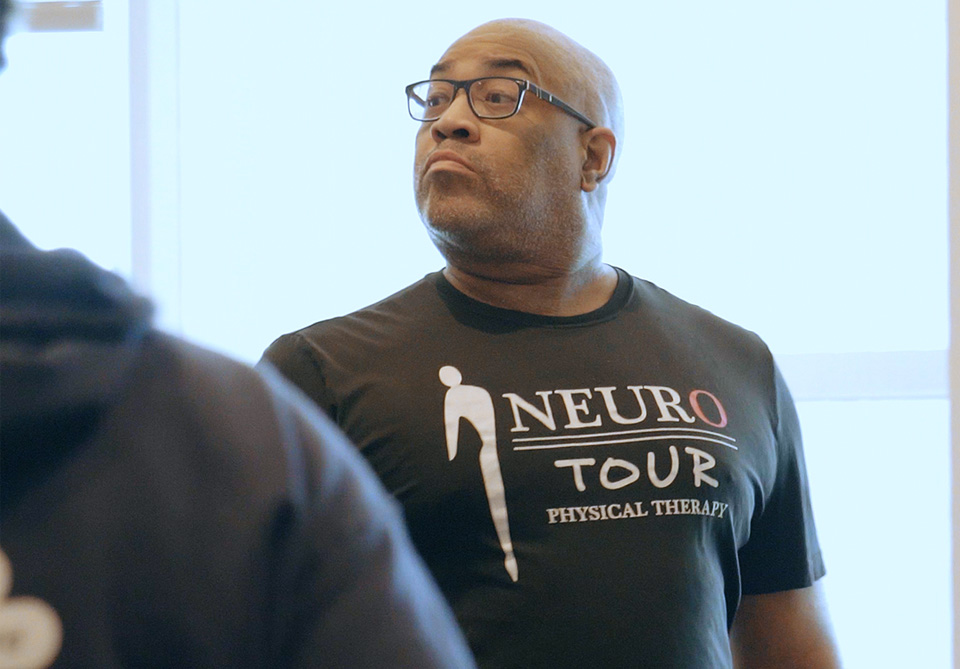 Man in glasses wearing a black T-shirt with logo and text 