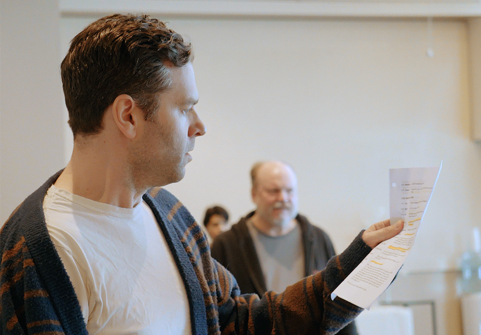 A man holding and reading a script with highlighted text in a rehearsal room 