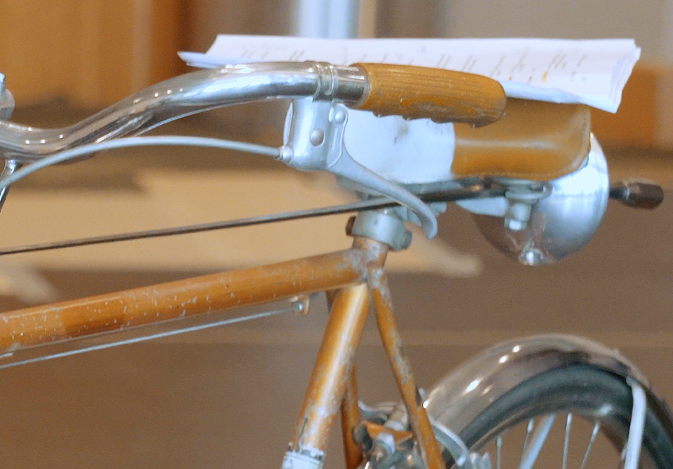 Close-up of a vintage bicycle handlebar with a script resting on it and a headlamp attached below.