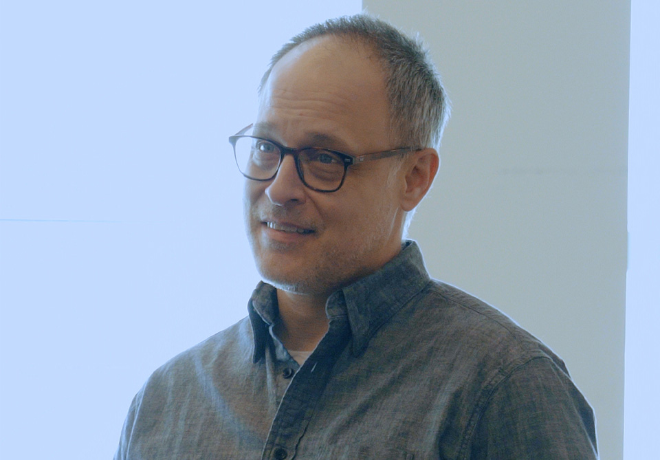 A person with glasses wearing a dark gray shirt in front of a light background.