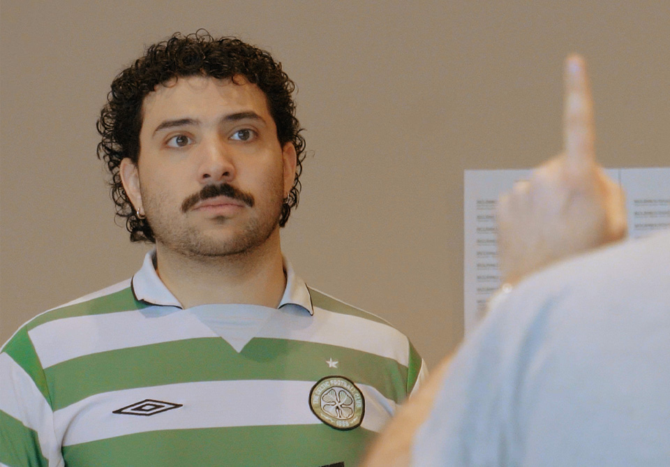 A man in a green and white striped jersey looks ahead as a blurred finger points toward him.