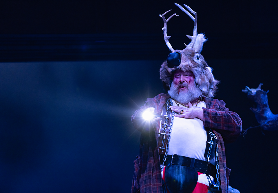 A person in a costume with antlers and a light, performing on stage with a dark background.