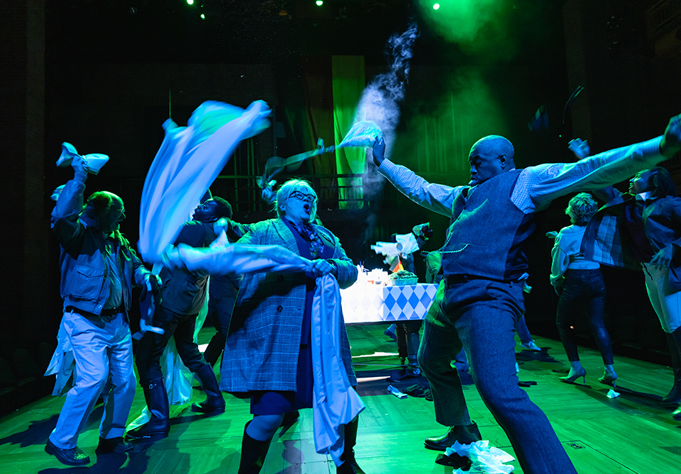 Performers on stage energetically waving cloths under blue and green lighting.